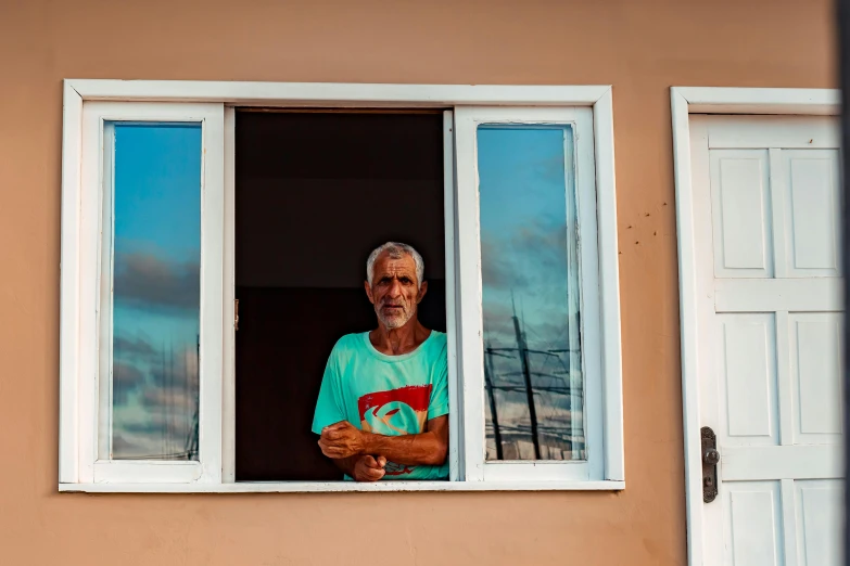 a man wearing a blue shirt standing in front of a window