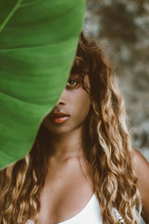 a woman with long curly hair is posing under a huge green leaf