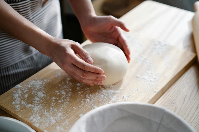 hands kneading a round dough on a wooden  board