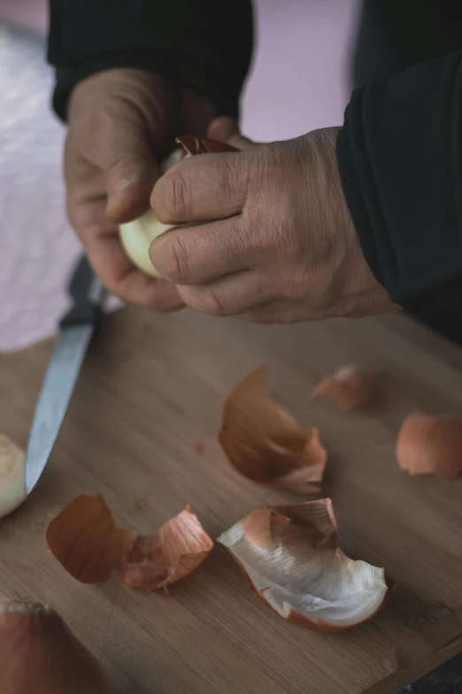 a person that is peeling an onion on a  board