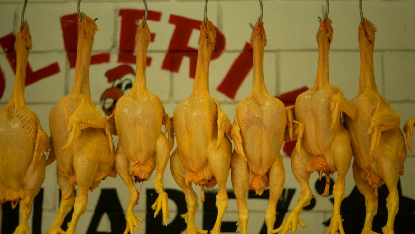 roasted chickens hang from hooks in front of graffiti