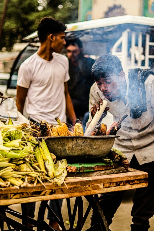 several people grilling corn and corn on the cob at an outdoor market