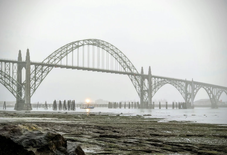 an ocean view with the tide crashing near a large bridge