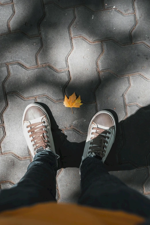 a person has their feet propped up on a sidewalk with a lone yellow leaf on it