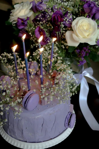 a birthday cake with candles lit sits in front of flowers and ribbon