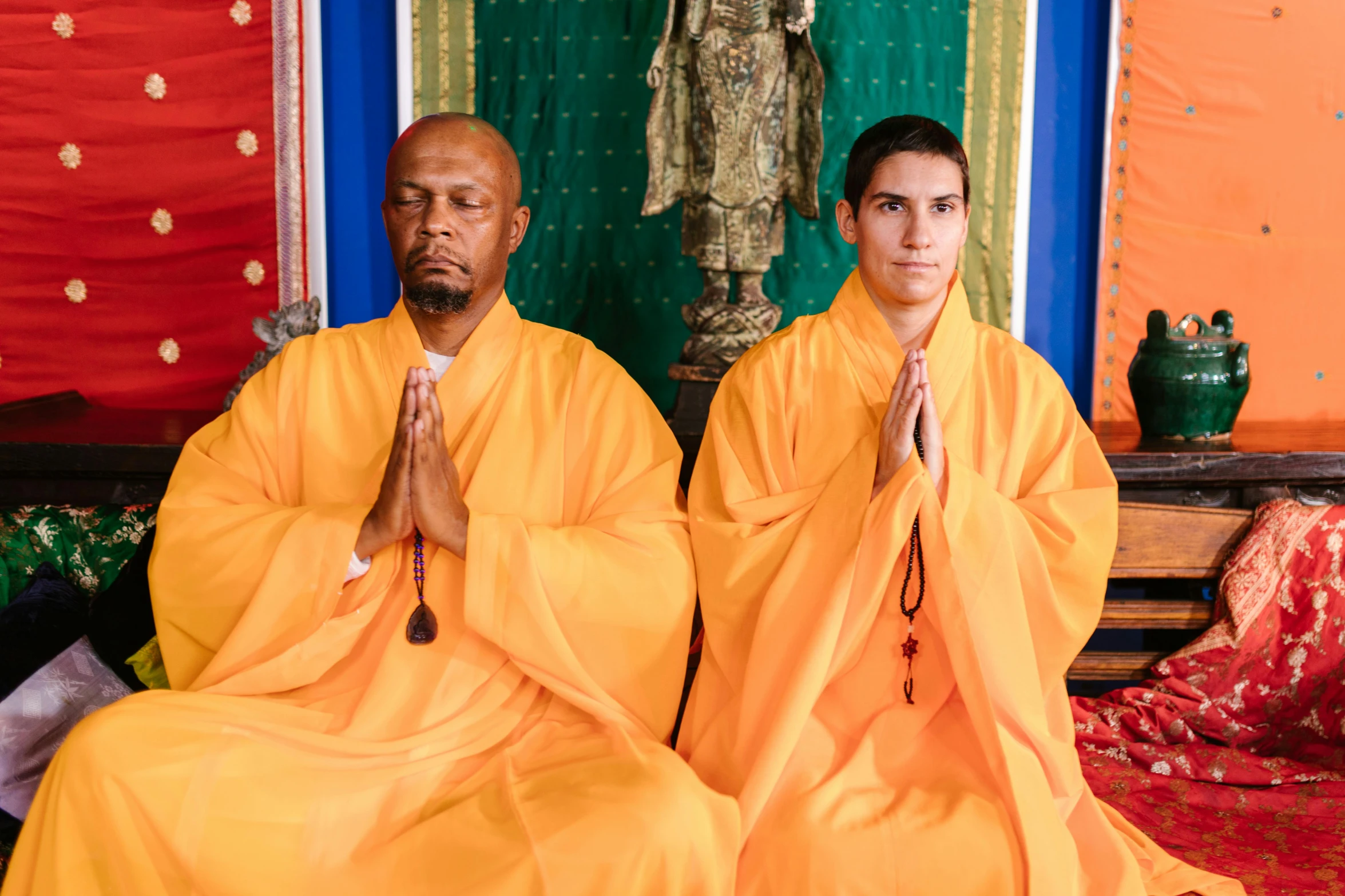 two people wearing orange robes meditating in a room