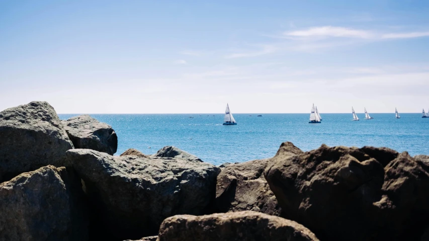 many small boats on the blue water near large rocks