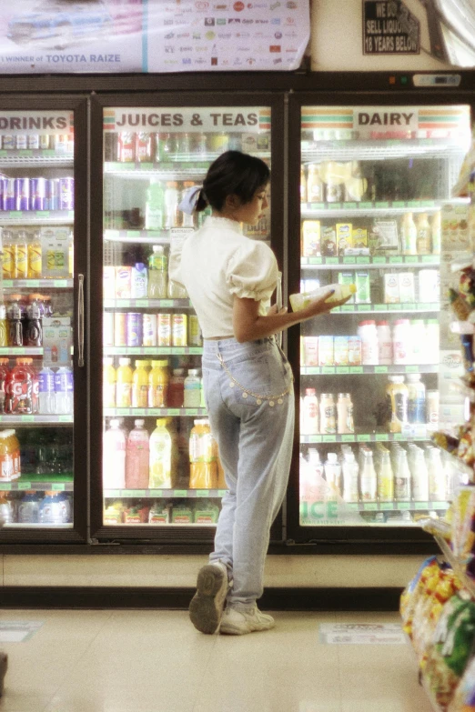 a woman in white shirt and jeans near refrigeration cabinets