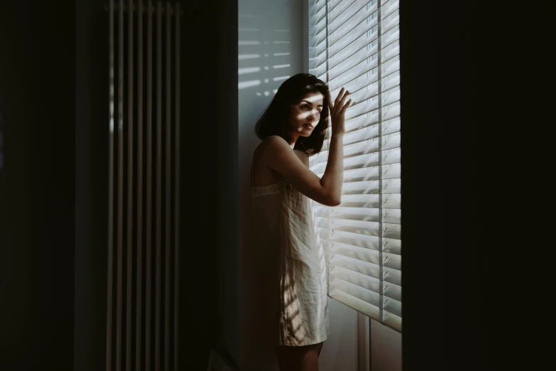 a woman leaning against a window that has blinds