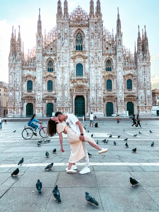 a woman in a beige dress kissing a man in front of a building