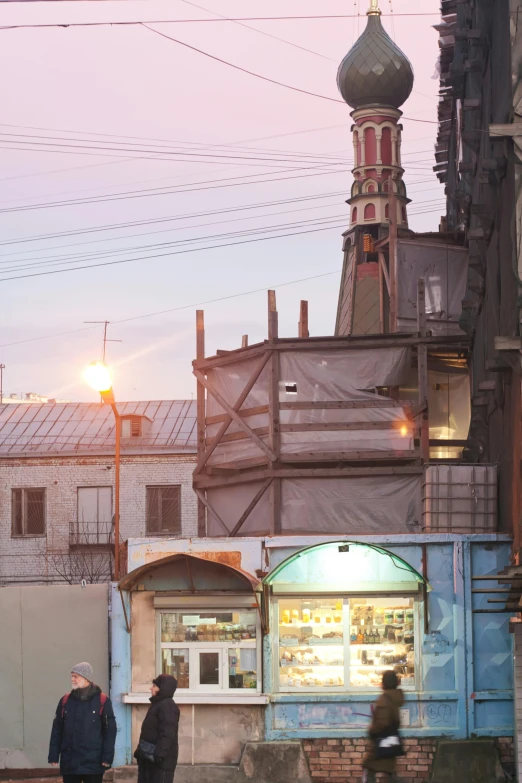 two people walking past some buildings in the evening