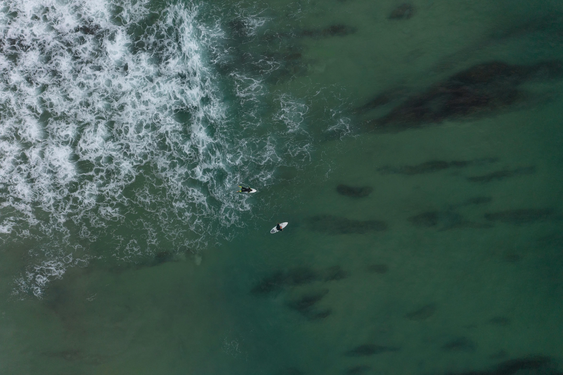 two surfers in the ocean on surfboards, looking down