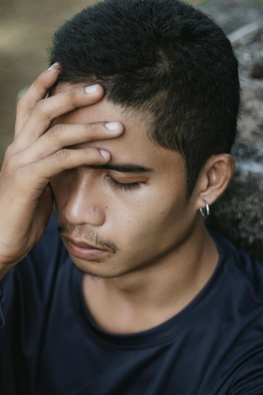 an asian man looks to his left with his hand on his head