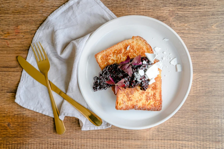 two pieces of toast and berries are on a plate with gold forks