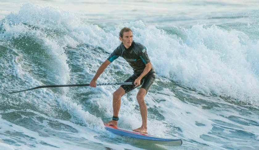 a man in wetsuit on surfboard holding pole while riding waves