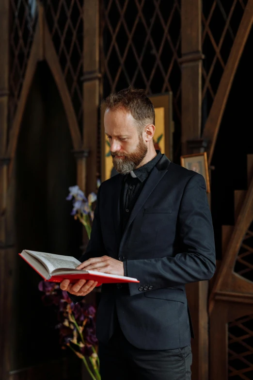 man in suit and tie reading in front of a wooden structure