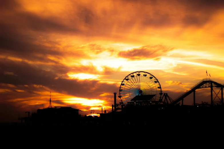 a silhouette of ferris wheel, a roller coaster and an evening sky