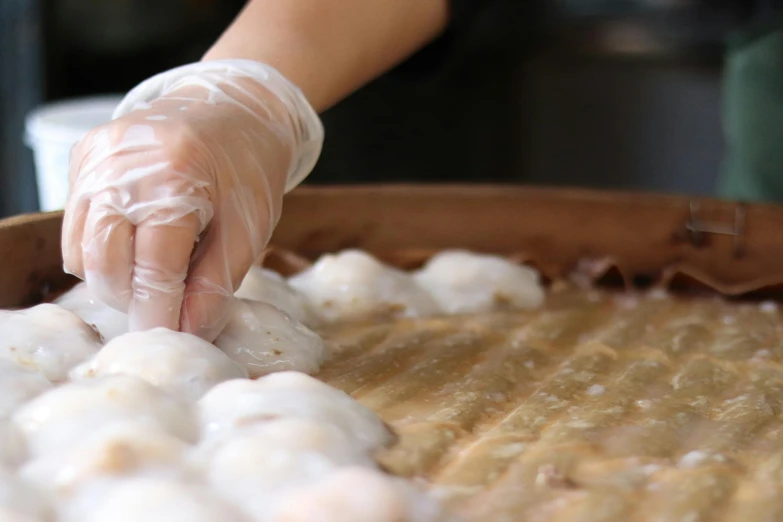 a woman with gloves holding up some dough on top of a pan