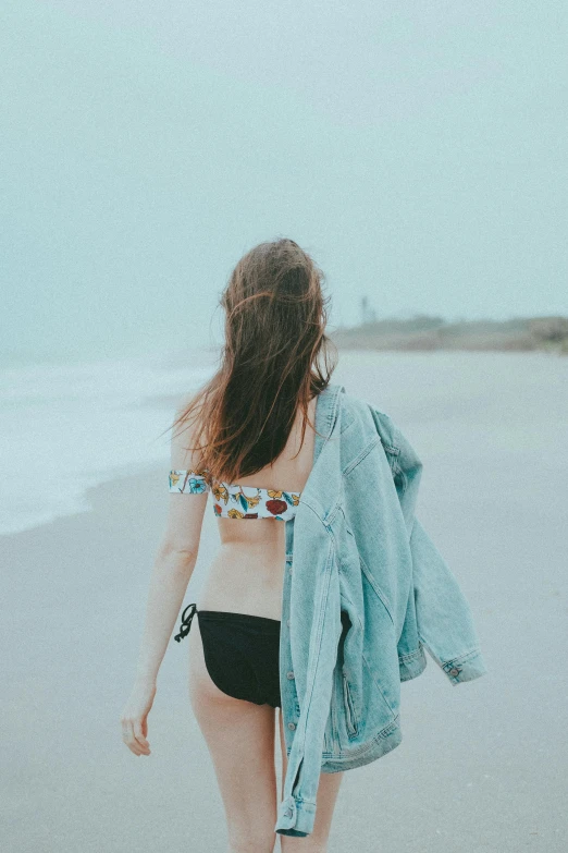 the woman is walking along the beach with a jacket