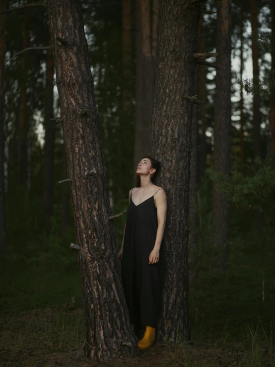 woman in a black dress standing next to a large tree