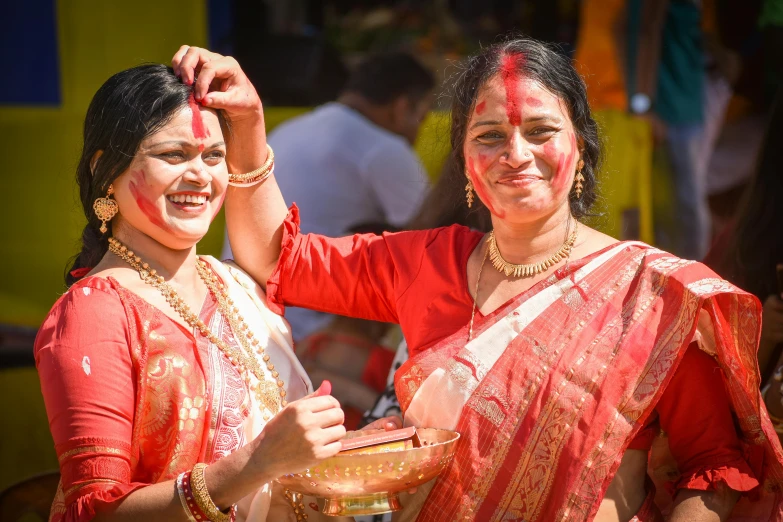 two women in red saris with white paint on their faces