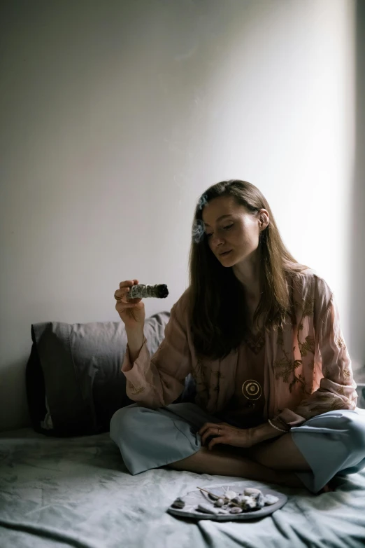 a person sits on a bed holding a cigarette in one hand