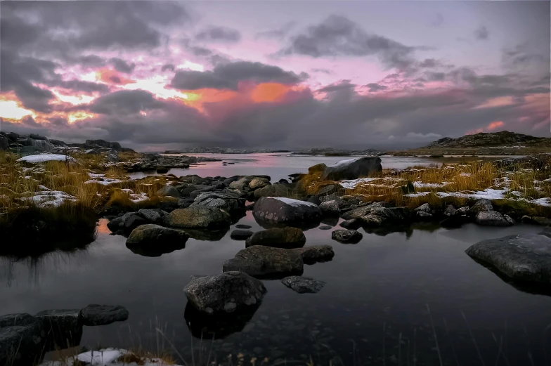 a lake surrounded by rocks with a few snow on the ground