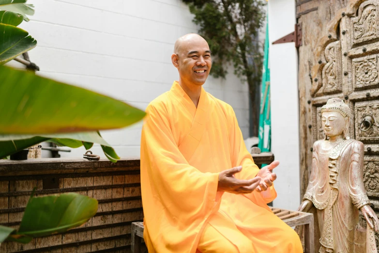 a smiling man in an orange robe sits on a wooden statue