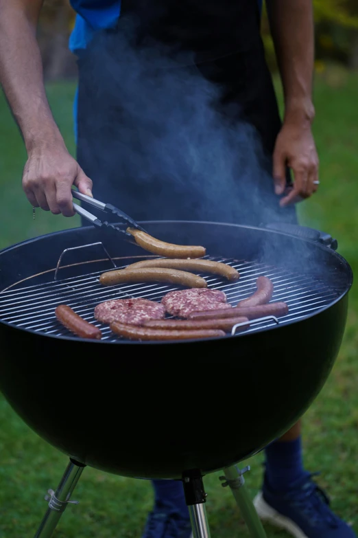 two people are standing over an open grill cooking sausage