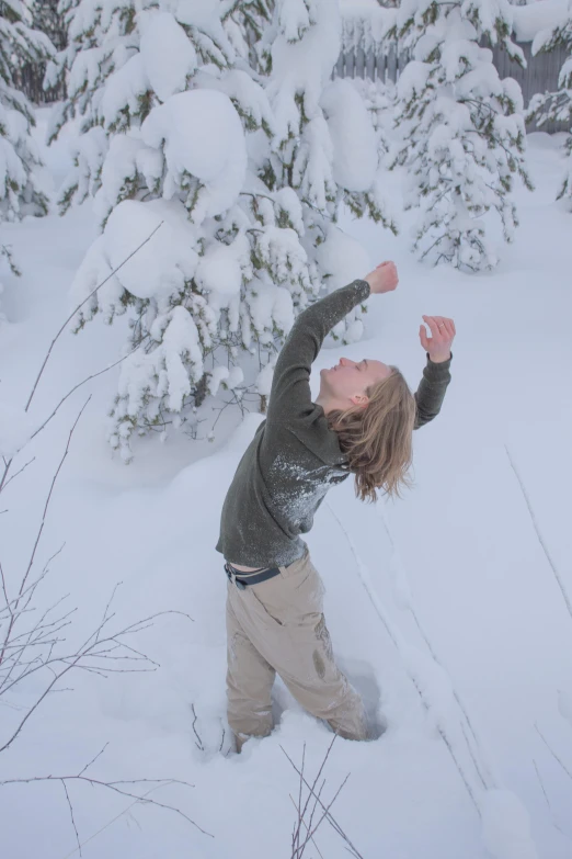 a woman standing in a field full of snow in front of a tree