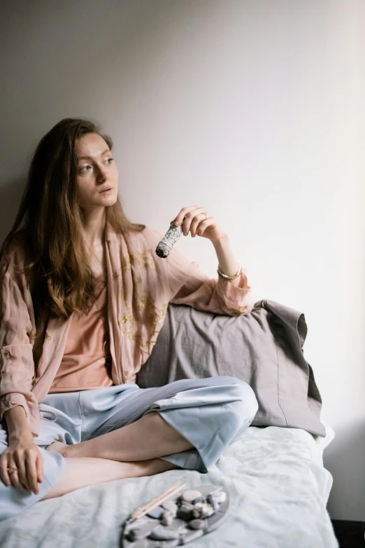 a girl with a pink sweater sits on a bed holding a remote control