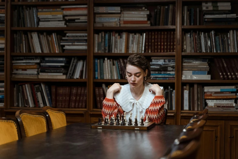 a woman in white top sitting at table with chess pieces