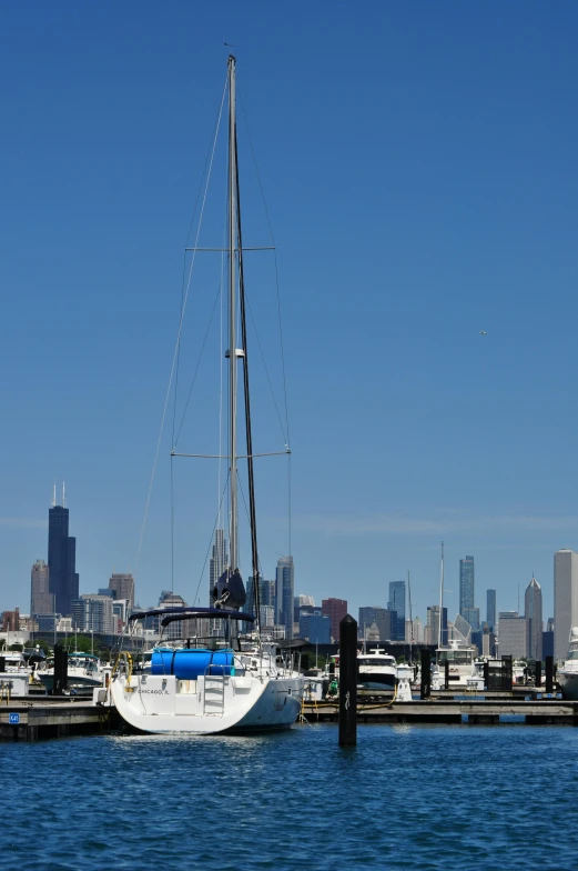 a white sail boat sailing in the harbor in front of a city