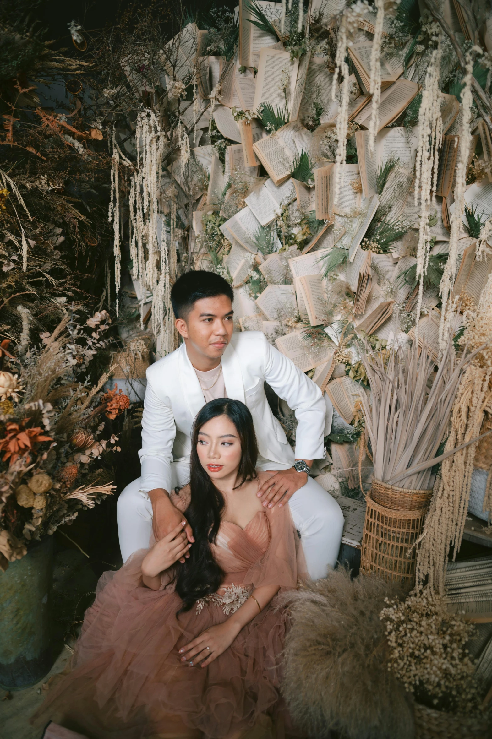 a man and woman sitting on the floor with a backdrop of feathers