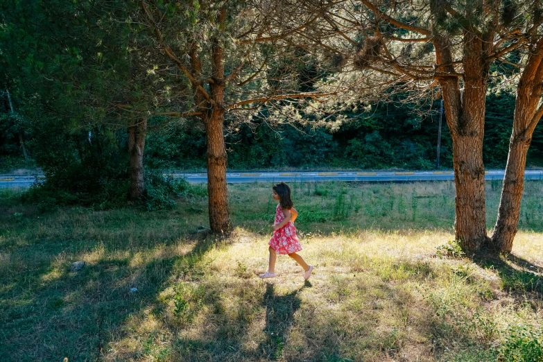 a girl in a pink dress walking by some trees