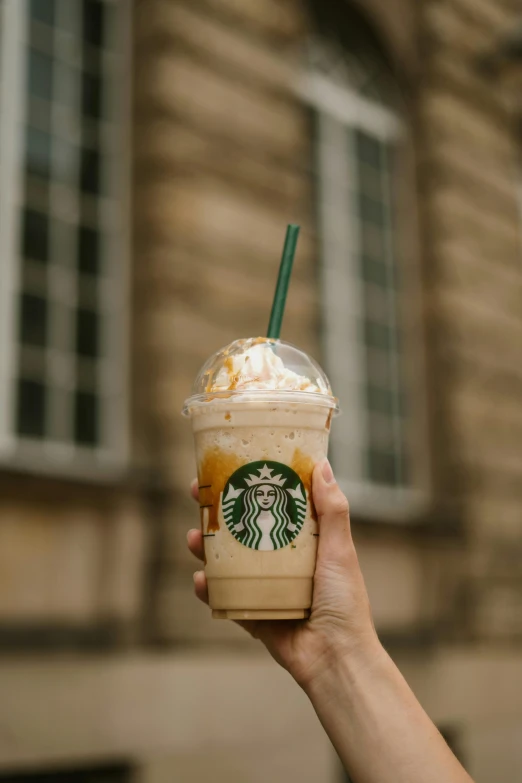 a person holding up a starbucks drink in front of a building