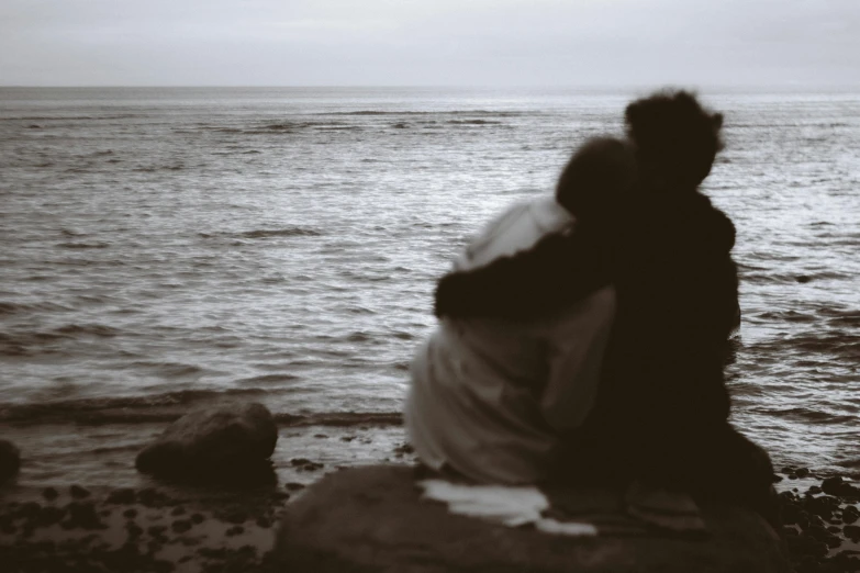 man and woman are sitting on a rock and the water is very calm