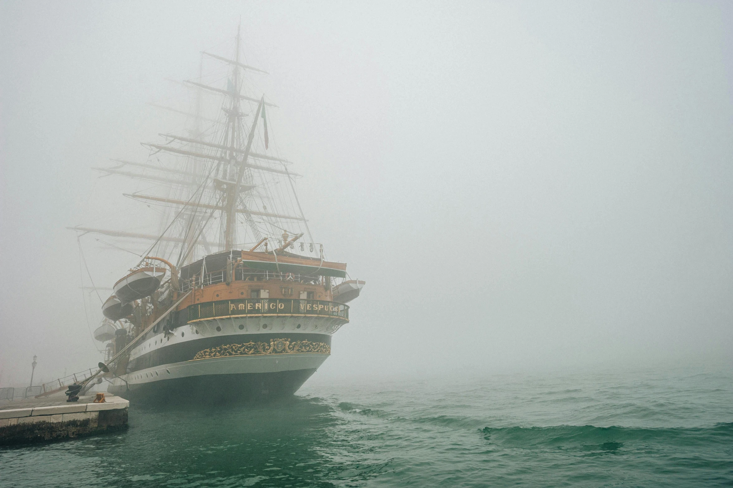 a large white ship with a brown sail sitting in the fog