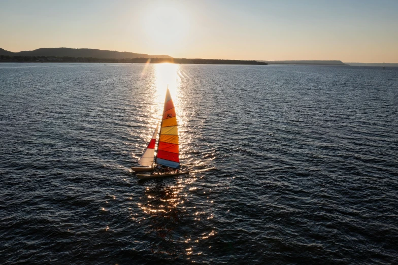 a sailboat is out on the water with the sun setting