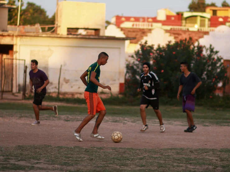 three young men are playing soccer in the dirt