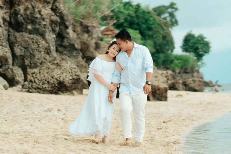 a man and woman standing on the beach by a tree