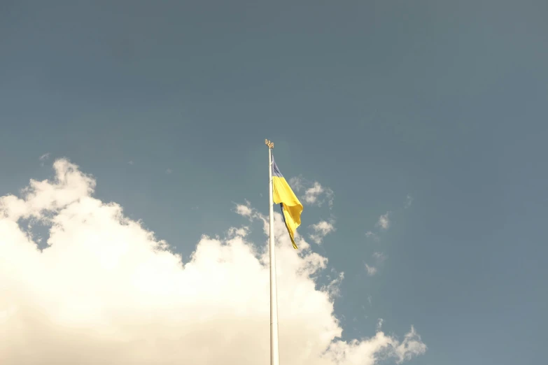 a flag pole with two flags on top and a cloudy blue sky behind