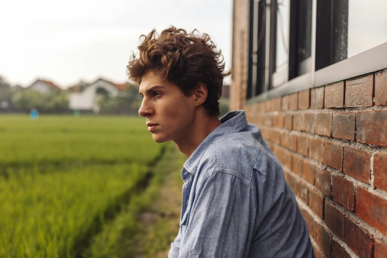 a young man standing in front of a brick wall looking off