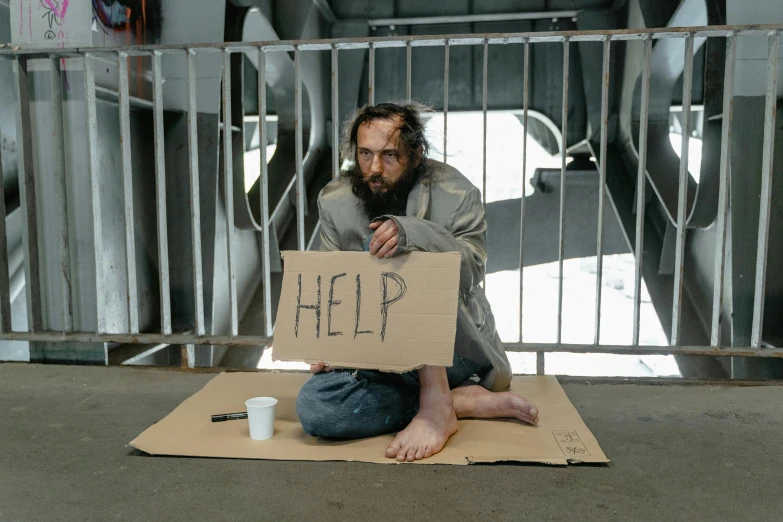 a man sitting on the ground with a cardboard sign saying help