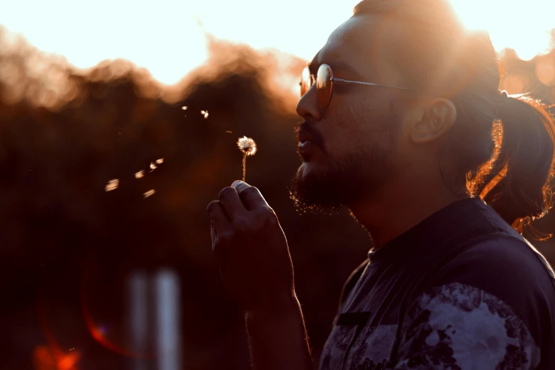 man blowing a dandelion in front of sunlight