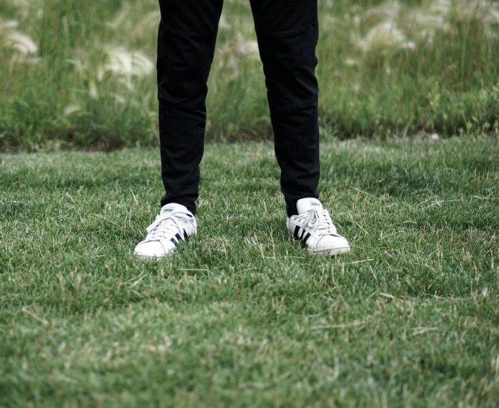 person with white sneakers on grass near grassy area