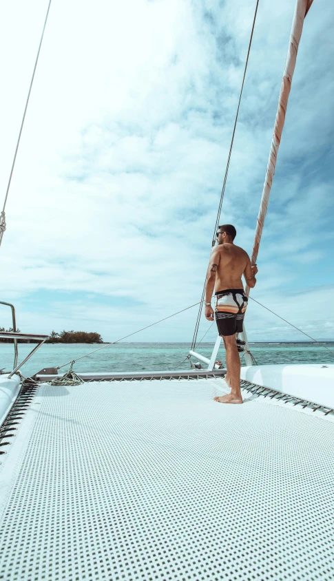 a shirtless man on the front deck of a sailboat