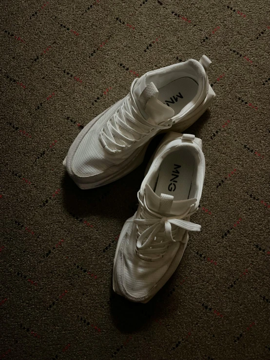 pair of white tennis shoes sitting on a carpeted floor