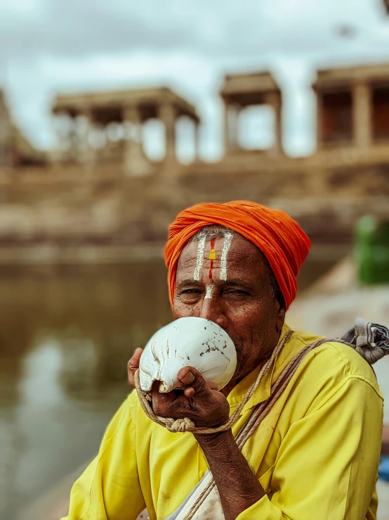 an old woman with an orange turban on her head drinking from a small round jug