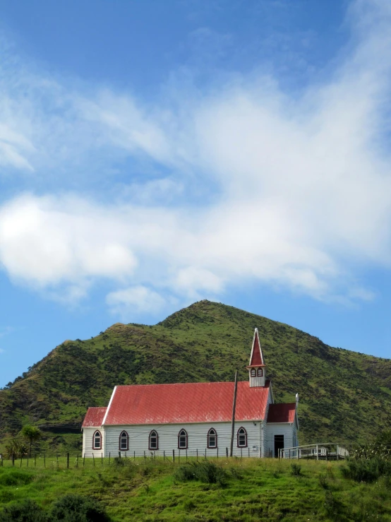 an old red and white church next to a hill